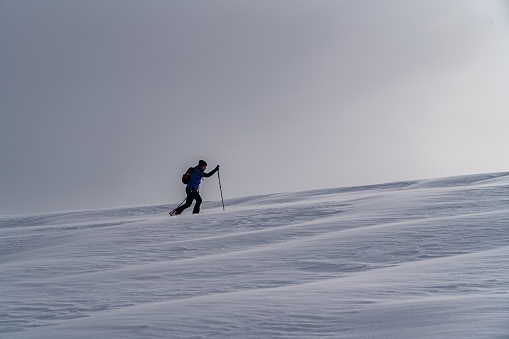 A skier climbing a hill on a cold winter day under a dark sky