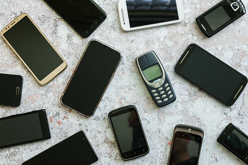 Flat lay depicting multiple generations of cell phone handsets on a textured stone surface.