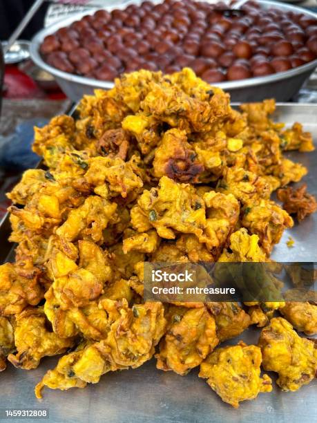Closeup Image Of Pile Of Crispy Onion Bhajis On Rectangular Catering Tray Indian Street Cuisine Vegetarian Snack Stainless Steel Bowl Of Gulab Jamun In Background Elevated View Focus On Foreground Stock Photo - Download Image Now