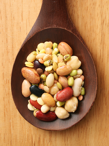 Top view of wooden spoon with a mix of soaked legumes on it