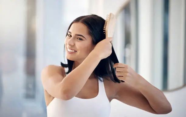 Hair, brush and bathroom with a woman in her home, brushing her hairstyle for haircare or treatment. Mirror, wellness and luxury with a female using cosmetic shampoo or keratin on her head in a house