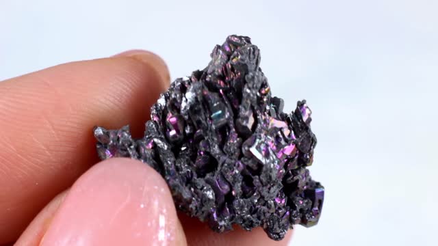 Woman hand holding shiny black Carborundum crystal (Moissanite or Silicon Carbide) on light background close up