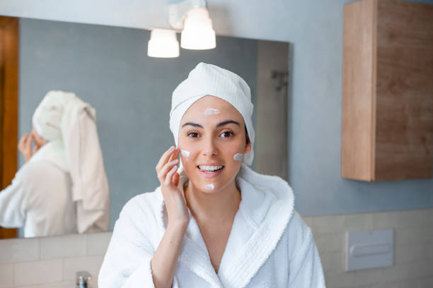 istock Woman in bathrobe applying cream on face in bathroom 1459316120