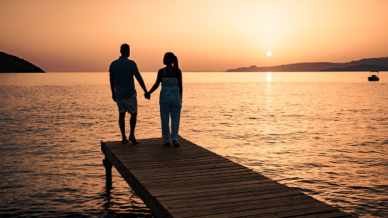 a couple standing on a wooden jetty, looking at colorful sunset on the sea, men, and women watching a sunset in Crete Greece Europe