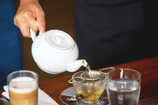 Pouring hot water through a tea strainer into a tea cup