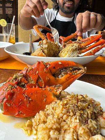 Stock photo showing freshly baked crab claw pincer served with rice, delicious crab meat made, butter and garlic sauce served in shell at restaurant in India. A man is eating his own crab meal in the background.