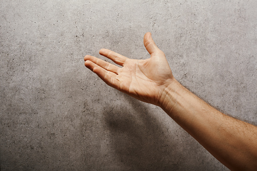 Male hand raised in front of a gray wall pleading