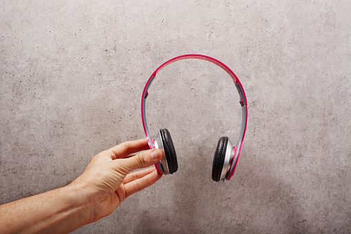 Hand holding  pink headphones in front of a gray wall