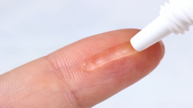 Transparent moisturizing gel applying on woman finger close up on light background