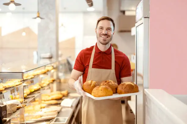 Bakery shop owner with loaf of bred smiling to the camera while standing at pastry shop