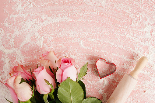 Heart, flowers and rolling pin on pink table background with copy space. Valentine's day cooking