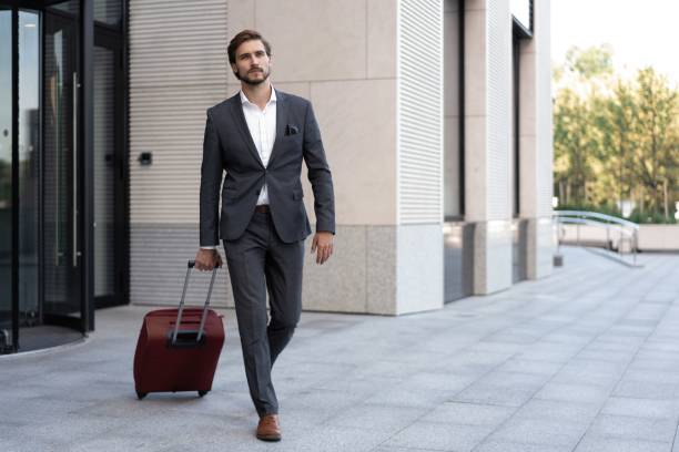 istock Smiling and good looking manager with suitcase walking outside modern office. 1459325911