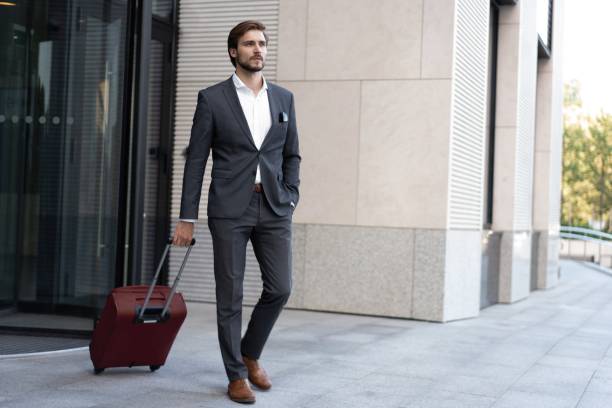 istock Smiling and good looking manager with suitcase walking outside modern office. 1459325912