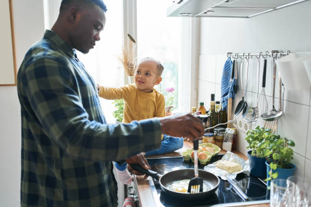 istock Father preparing egg in frying pan with son sitting by over kitchen counter 1459326173