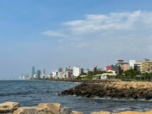 Photo of Image of view at Mount Lavinia beach in Colombo, Sri Lanka, sandy and rocky beach with, sea and capital city visible in background, coastal erosion defences and blue sky on sunny day