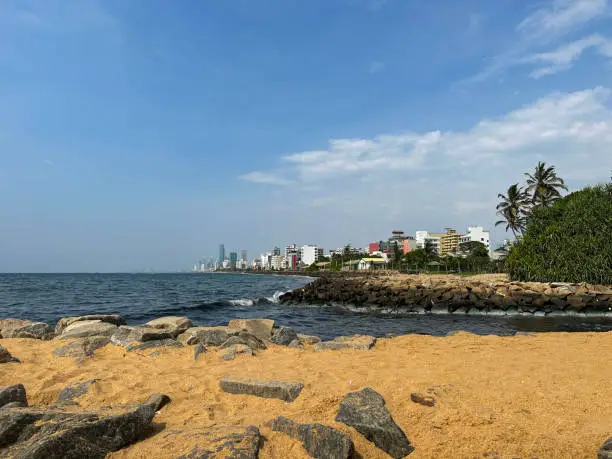 Photo of Image of Mount Lavinia beach in Colombo, Sri Lanka, sandy and rocky beach with sea and capital city visible in background, coastal erosion defences and blue sky on sunny day