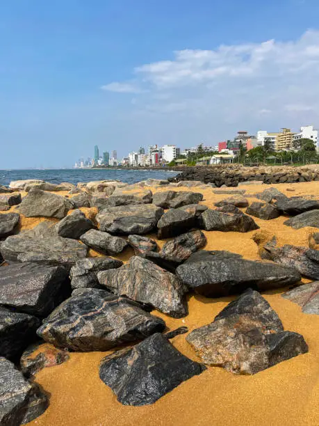 Photo of Image of rock armour / rip rap at Mount Lavinia beach in Colombo, Sri Lanka, sandy and rocky beach with sea and capital city visible in background, coastal erosion defences and blue sky on sunny day