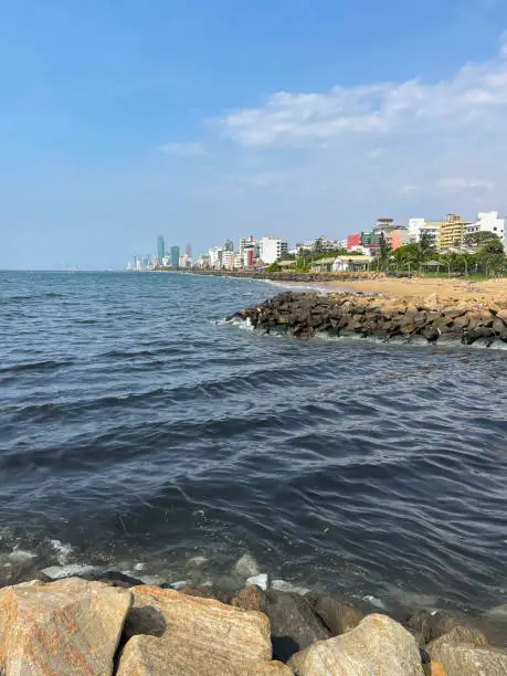 Photo of Image of view at Mount Lavinia beach in Colombo, Sri Lanka, sandy and rocky beach with, sea and capital city visible in background, coastal erosion defences and blue sky on sunny day, vertical