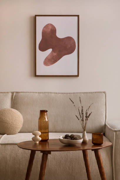 istock Creative composition of living room interior with mock up poster frame, modern beige sofa, oval wooden coffee table, round pillow, glass case, craetive bowl with dried fruit, sculpture and personal accessories. Home decor. Template. 1459326965