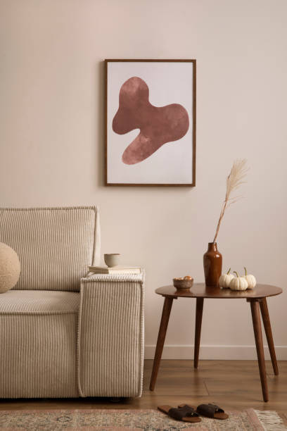 istock Creative composition of living room interior with mock up poster frame, modern beige sofa, oval wooden coffee table,  round pillow, glass case, craetive bowl with dried fruit, sculpture and personal accessories. Home decor. Template. 1459327039