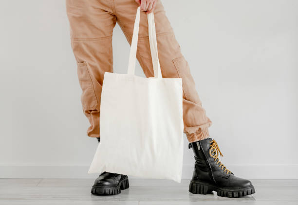 Girl with cotton linen eco bag mockup Girl in boots and pants holding cotton linen eco bag mockup. Woman legs with environment friendly shopping handbag with empty copy space for business tote bag mock up stock pictures, royalty-free photos & images