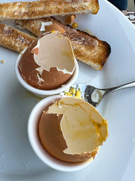 istock Full frame image of buttered toast soldiers with two empty eggshells in egg cups on white plate, eaten soft boiled egg with runny yellow yolk, metal teaspoon, elevated view 1459329574