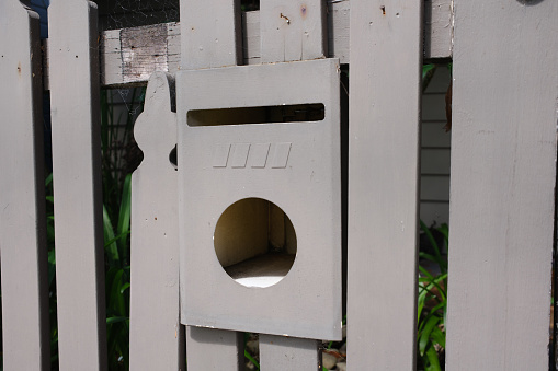 Cream colored metal mailbox on a fence.;