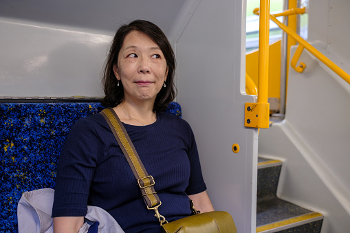 Japanese woman sitting on a train looking to the side.