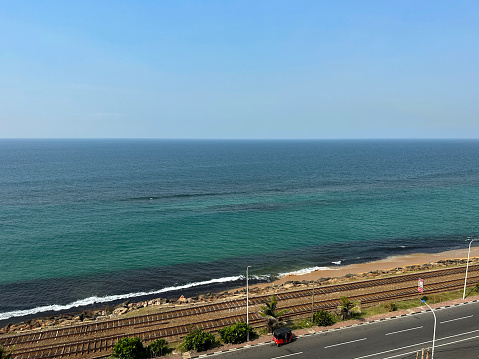 Stock photo showing aerial view of metal railway the line and gravel of southern line diesel railroad track in Colombo, Sri Lanka running parallel to the coast with waves breaking on the rocky shore.