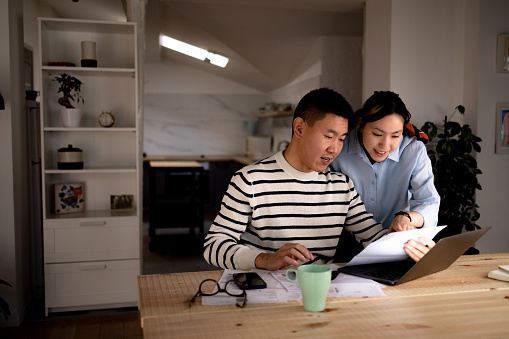 Young Asian couple cooperating while going through their financial bills at home.