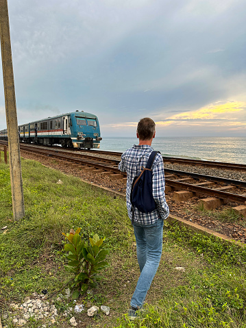 Stock photo showing close-up view of metal railway the line and gravel of southern line diesel railroad track in Colombo, Sri Lanka running parallel to the coast with waves breaking on the rocky shore.
