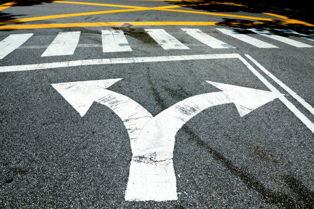 Forked road arrow sign and crosswalk on asphalt road Directional sign on city road in Kuala Lumpur fork in the road stock pictures, royalty-free photos & images