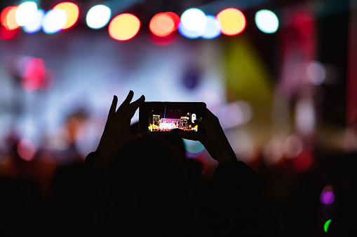Person holding smartphone and silhouettes of concert crowd with stage lights