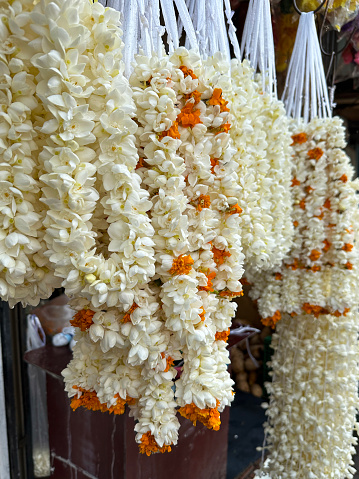 Stock photo showing a close-up view of white jasmine garlands for sale hanging on a market stall display.