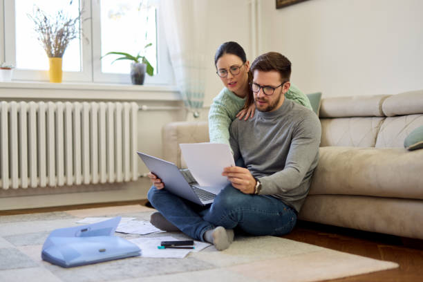 Couple sitting in their living room and checking their finances using laptop stock photo
