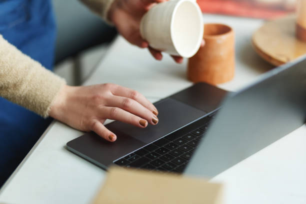 istock Potter entrepreneur using laptop in workshop, hands only, holding ceramic cup in hands, takes orders online 1459343545