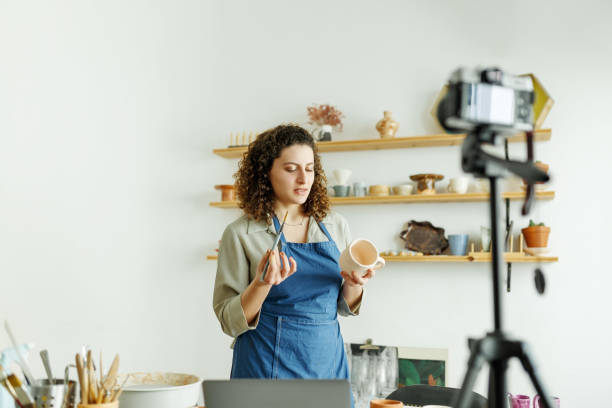 istock Females potter making a vlog, recording online course, lessons in her studion with earthenware shelf on background 1459343559