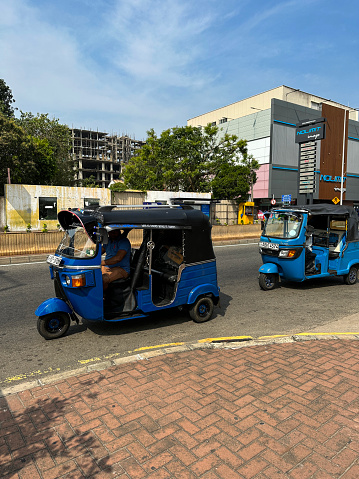 Colombo, Sri Lanka - January 16, 2023: Stock photo showing a view of a street in downtown Colombo with blue and black auto rickshaws driving in retail area.