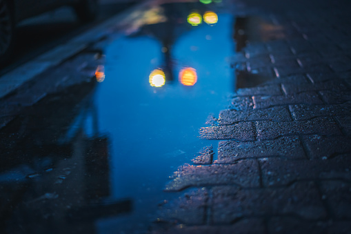 A puddle on the sidewalk in the city with the reflection of night city lights.