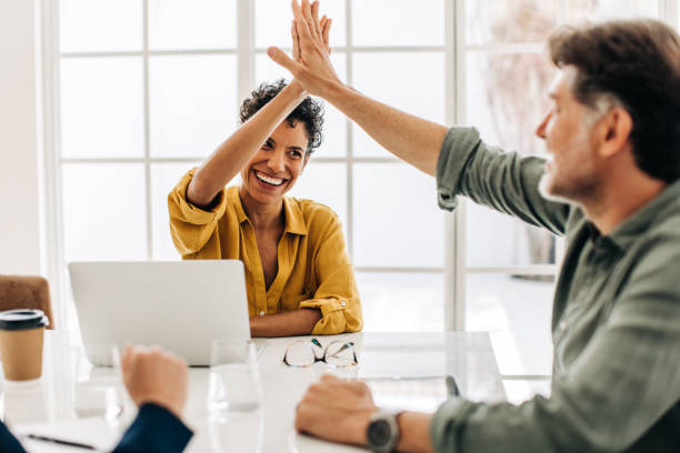 Business colleagues celebrating success in a boardroom Business colleagues celebrating success in a boardroom. Two happy business people doing a high five during a meeting in an office. Teamwork and goal achievement. high five stock pictures, royalty-free photos & images
