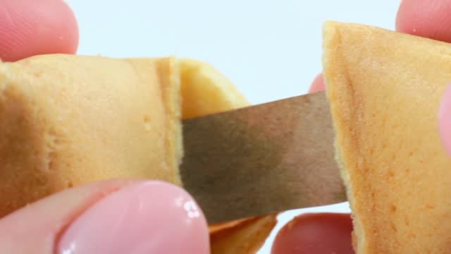 Woman hands opening a cracking yellow Chinese fortune cookie with a note on light background close up