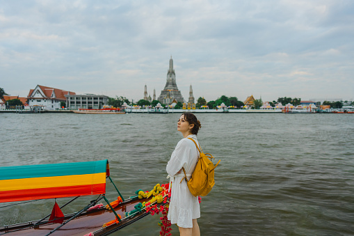 Young Caucasian woman looking at Wat Arun temple in Bangkok  from the riverside