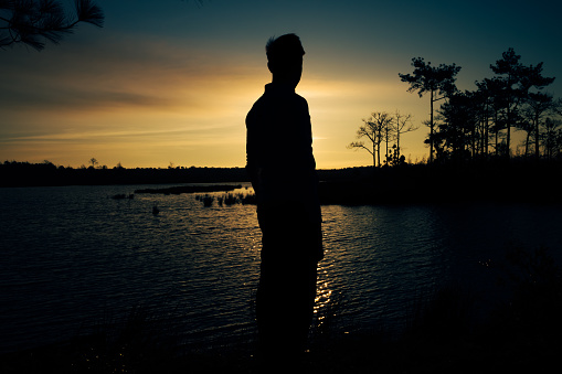 Silhouette of a man standing by the river to watch the sunset , Rear view.