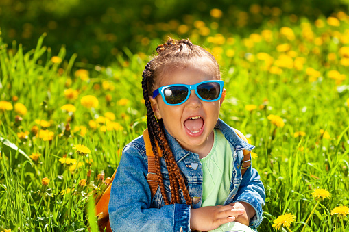 fashionable baby girl sitting in sunglasses in the grass on nature
