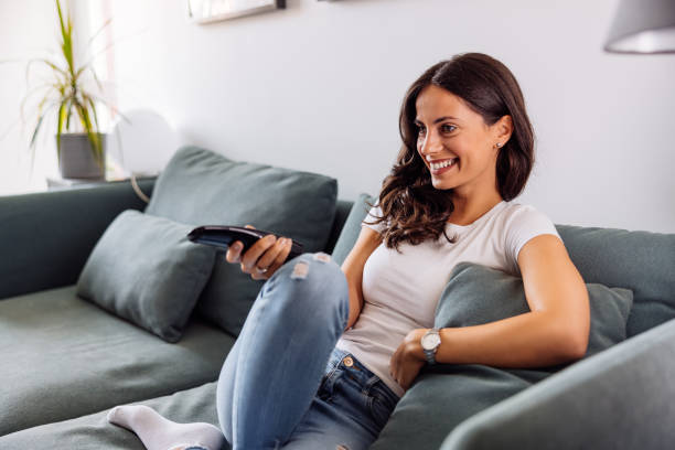 istock A smiling young woman sitting on the sofa and watching television. 1459354687
