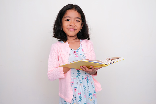 Asian little girl smiling at the camera when reading a book