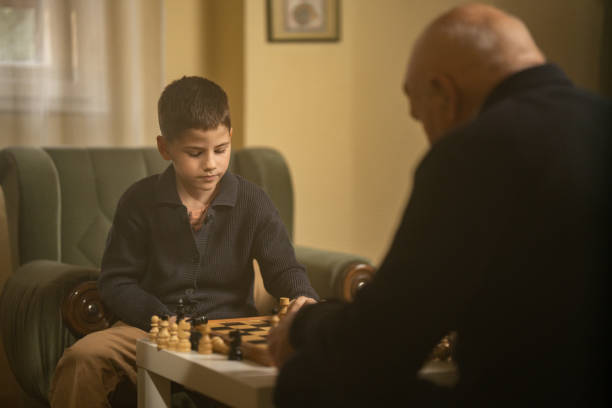 Old man playing chess against his young grandson in living room at home.
