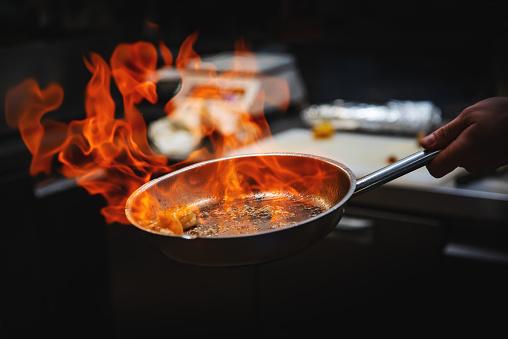 Chef hand in restaurant kitchen with pan, cooking flambe on shrimps