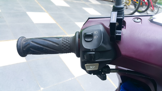 Close up view of horn button, turn signals, and lamp on left motorcycle handlebar. Outdoors.