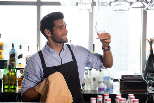 Young caucasian man is bartender cleaning and wipe glass with professional at counter, portrait handsome male preparation glass or wineglass, barman standing with confident at restaurant luxury.